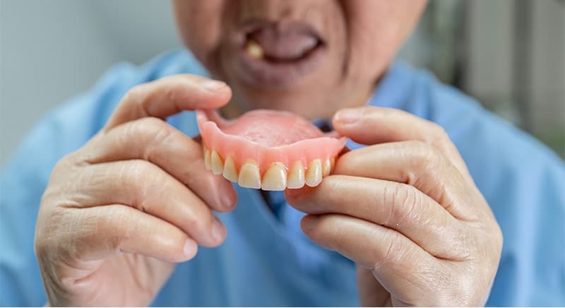 Patient holding a custom-fitted denture, showing natural-looking replacement teeth
